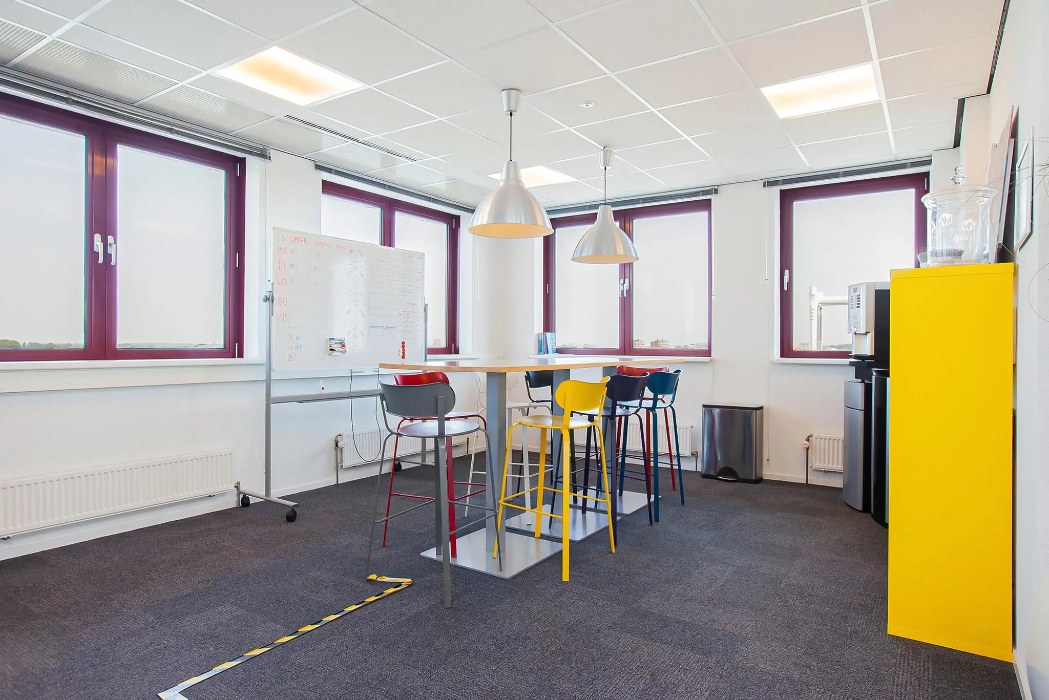 Moderne kantoorruimte aan de Laan der Verenigde Naties met hoge tafel, kleurrijke barkrukken en grote ramen.